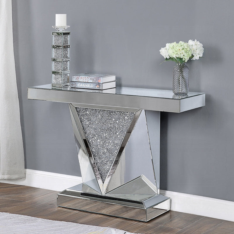Modern mirrored console table with a geometric V-shaped glitter panel, styled with decorative books, a candle holder, and a vase of white flowers.