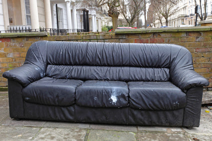Old worn black leather sofa left outdoors showing used furniture condition